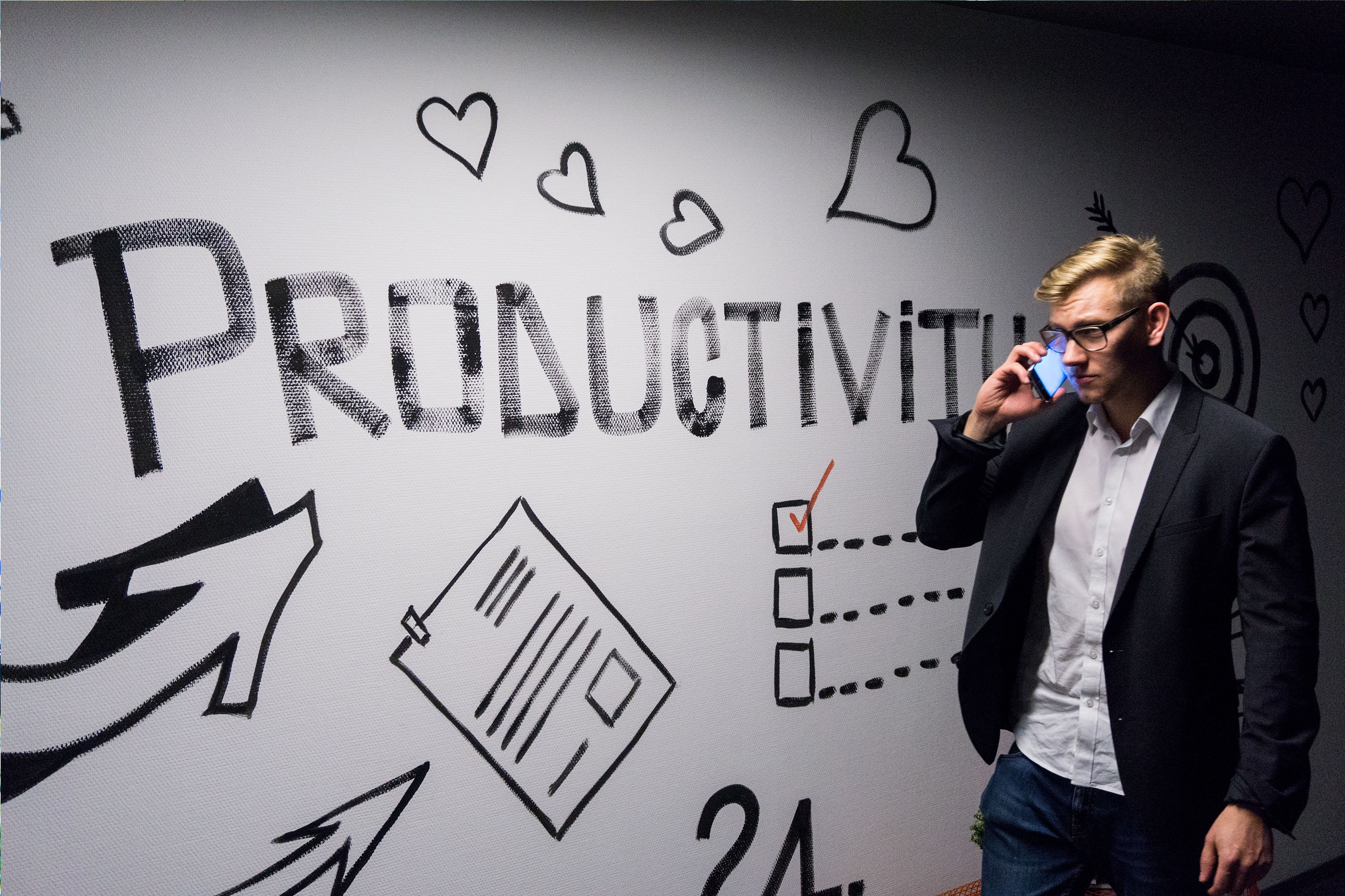 A businessman wearing a suit talks on the phone in front of a wall with "Productivity" painted on it.